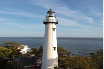 A white lighthouse stands tall on a backdrop of water and trees. Located on St. Simons Island