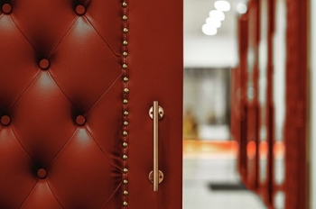 Close-up view of a partially open red leather door with a tufted, buttoned surface and decorative brass nailhead trim.
