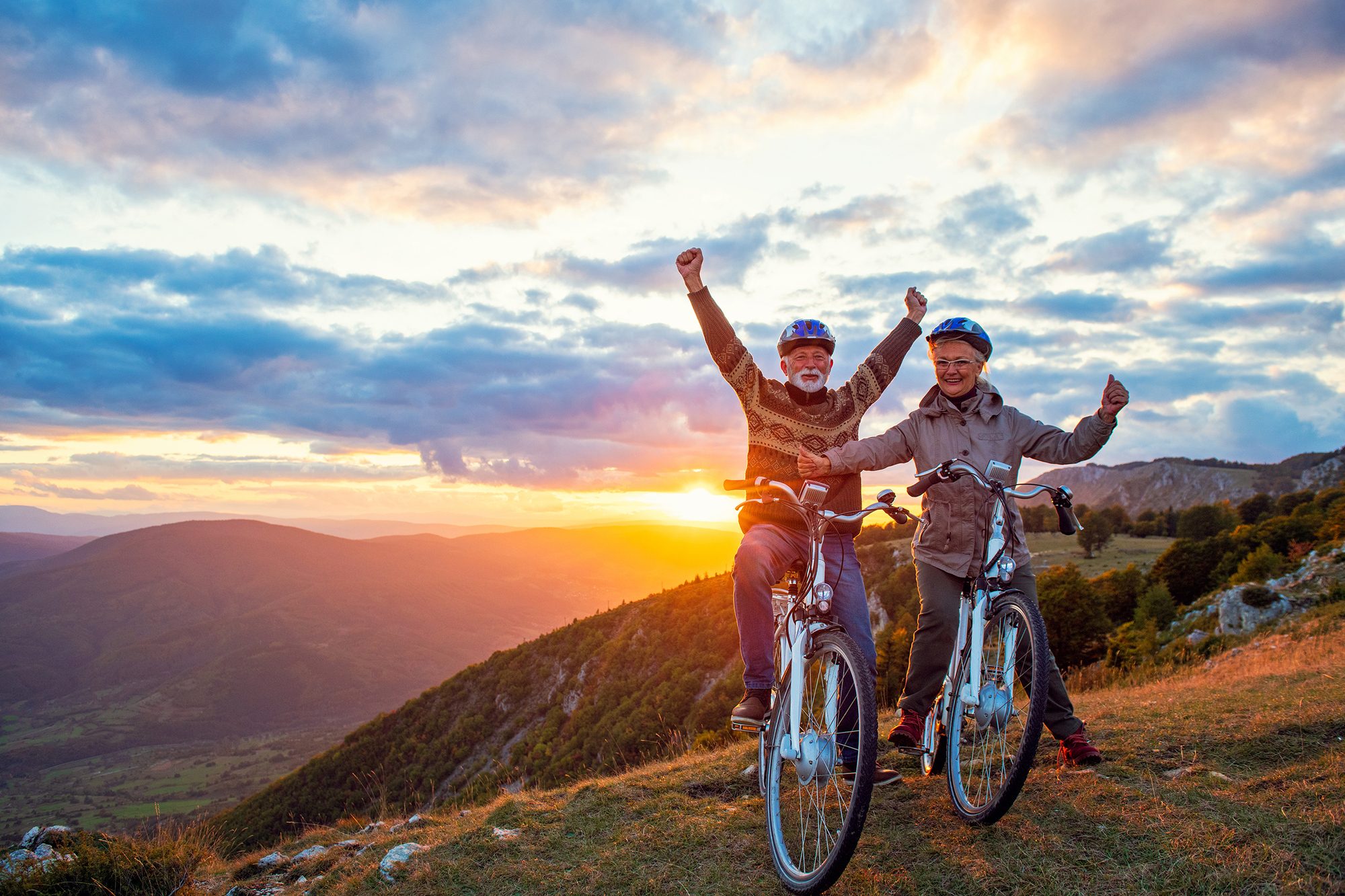 older couple biking on a mountain hilltop at sunset