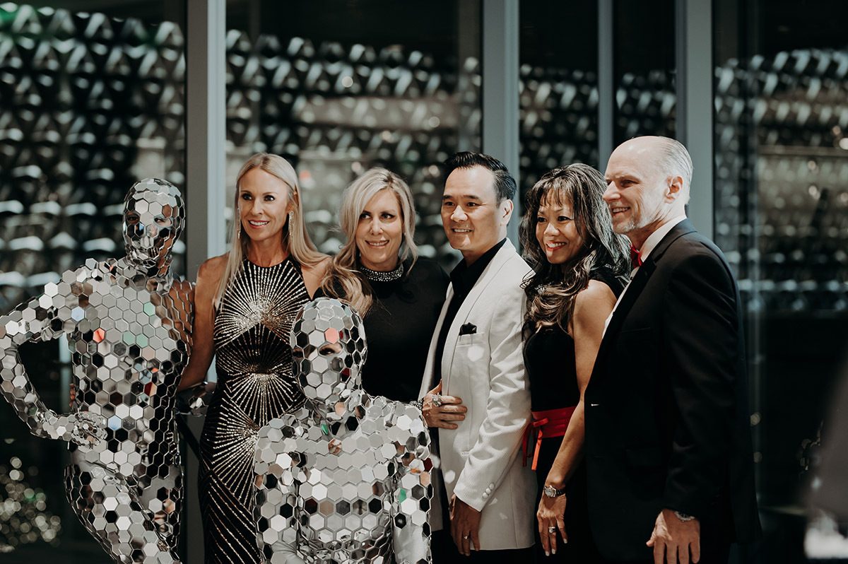 several clients posing for a photo with 2 people dressed in silver mirror outfits