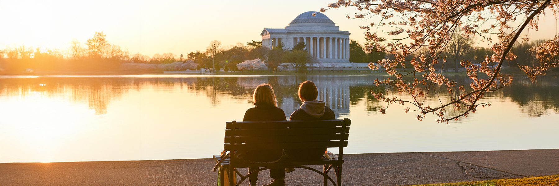 people sitting on bench overlooking lake and monument at sunset